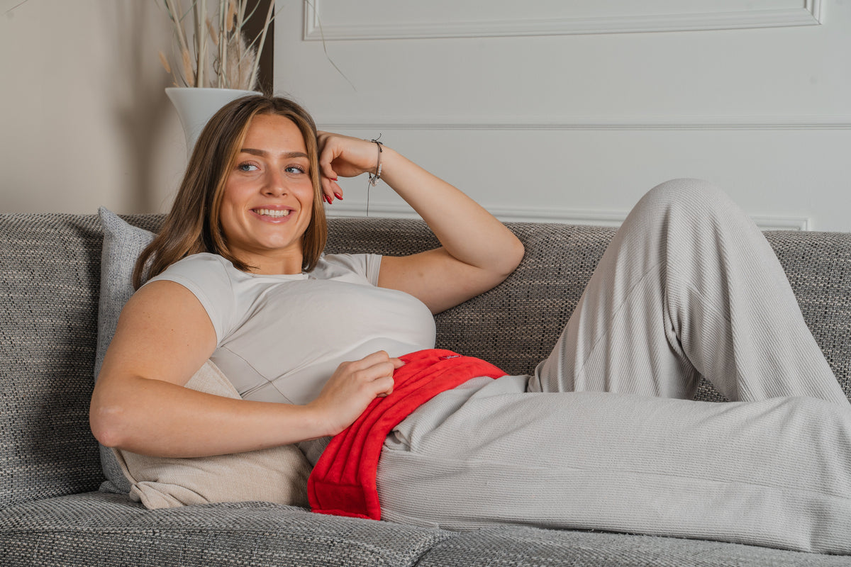 Vrouw ligt op de bank met een rood warmtekussen op haar buik